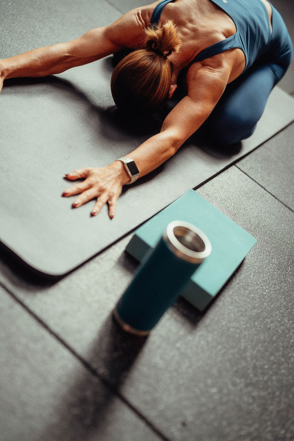 Woman stretching on a yoga mat with a drink and yoga block nearby