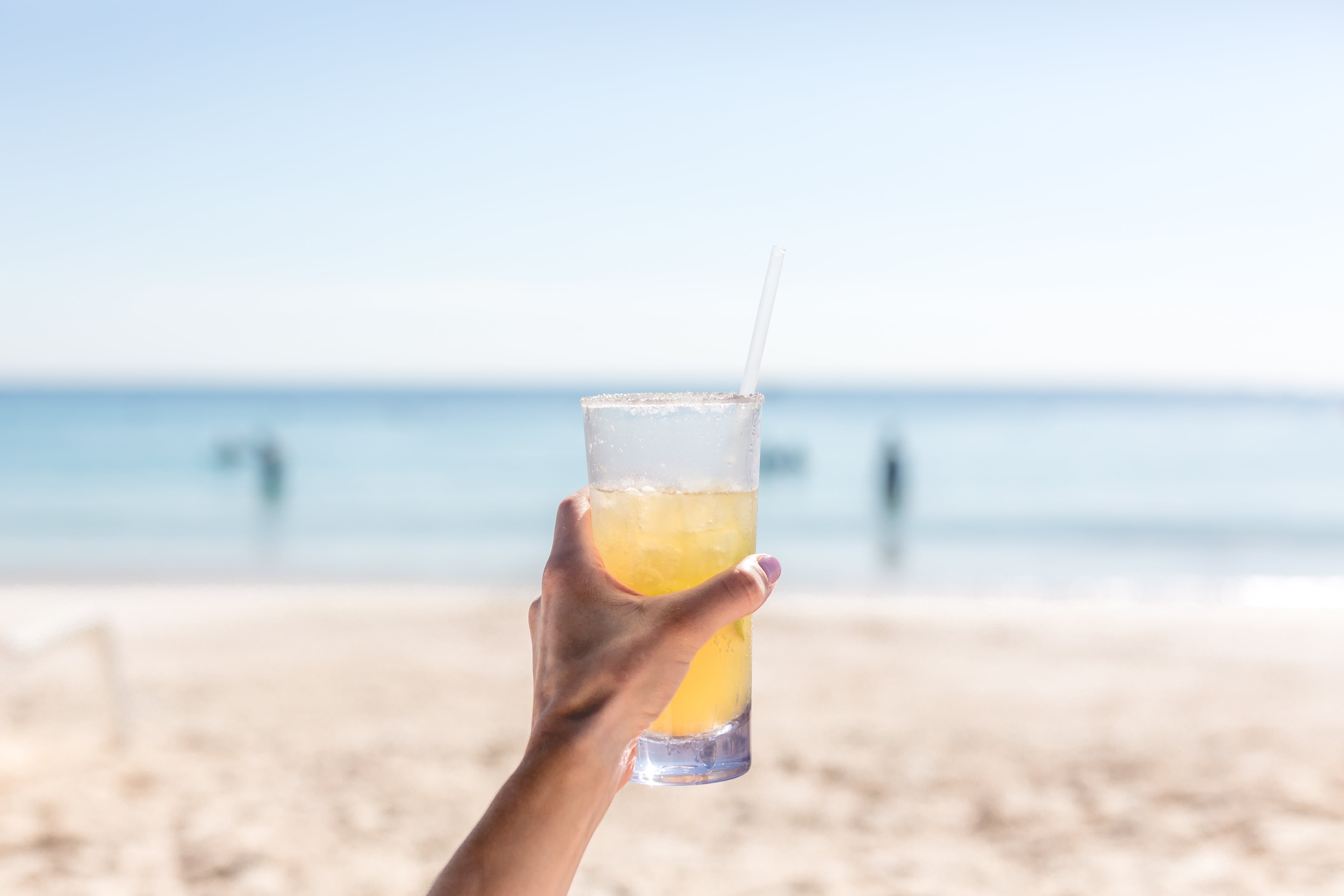 Hand holding a glass ofMove Blend on a beach with a blurred background