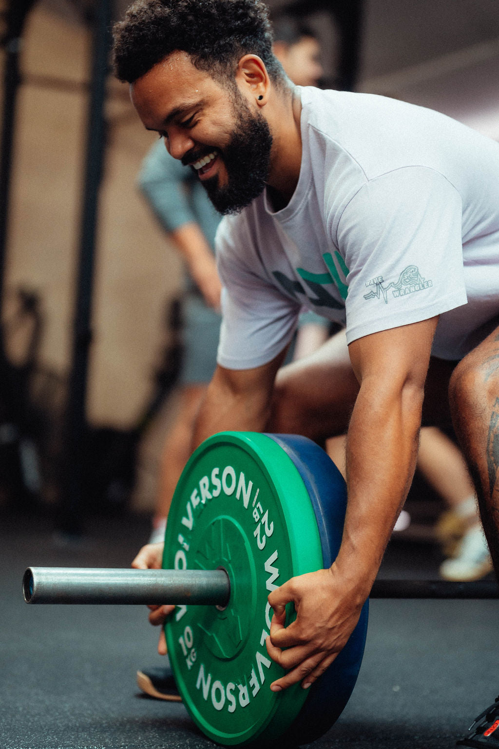 Happy man loading green and blue plates onto a barbell in a gym setting